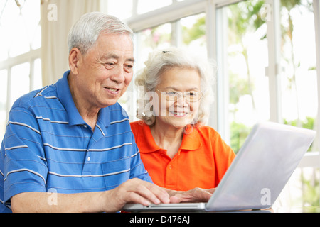 Senior Chinese Couple Sitting At Desk Using Laptop At Home Stock Photo