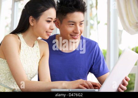 Young Chinese Couple Sitting At Desk And Using Laptop At Home Stock Photo