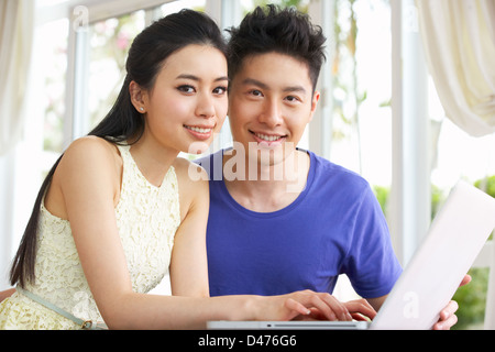 Young Chinese Couple Sitting At Desk And Using Laptop At Home Stock Photo