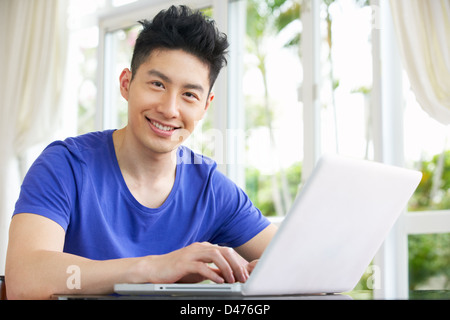 Young Chinese Man Sitting At Desk Using Laptop At Home Stock Photo