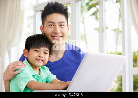 Chinese Father And Son Sitting At Desk Using Laptop At Home Stock Photo