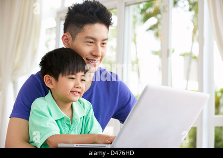 Chinese Father And Son Sitting At Desk Using Laptop At Home Stock Photo