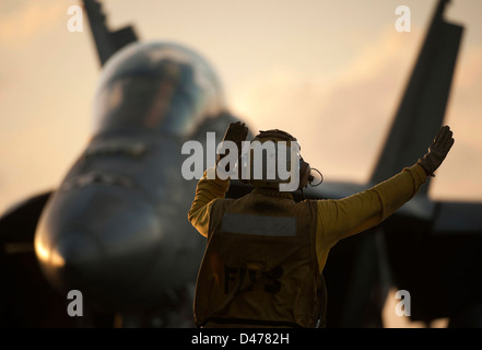 An aircraft director guides a jet to the waist catapults. Stock Photo