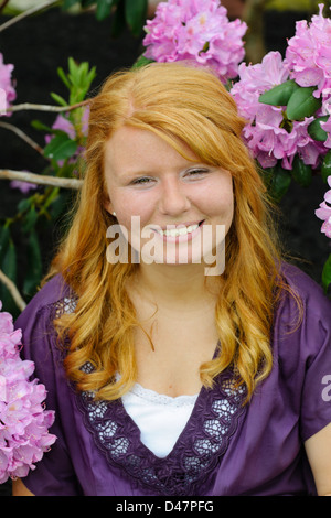 Smiling teen girl beside purple hydrangea flowers, red haired eighteen year old. Stock Photo