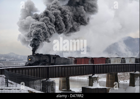 Steam train crossing bridge over Potomac River making tall smoke plume in the cold air, an old locomotive with vintage freight train. Stock Photo