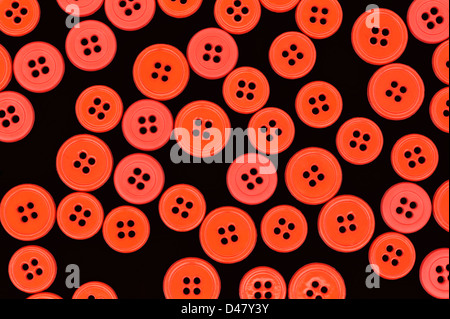 Orange and pink sewing buttons randomly scattered on a black background, a studio shot, top view. Stock Photo