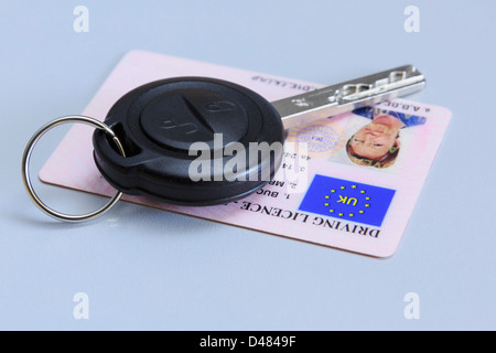 Remote car key with a woman's UK plastic card photographic driving licence on a plain blue background. Stock Photo