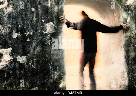 Adult male moving from darkness into light through portal. He is holding on to the stone wall. Stock Photo