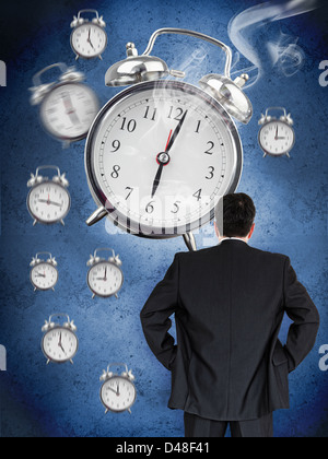 Businessman looking at wall of alarm clocks Stock Photo