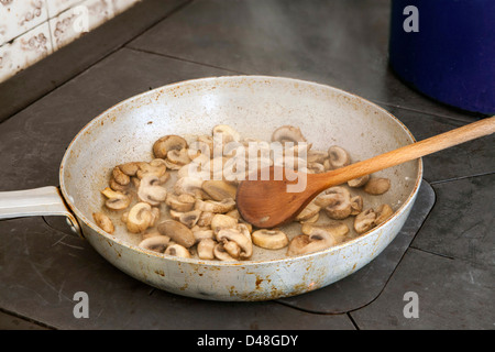 Fried mushrooms on a woodstove, stirred with wooden spoon Stock Photo