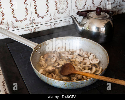 Fried mushrooms on a woodstove, stirred with wooden spoon Stock Photo