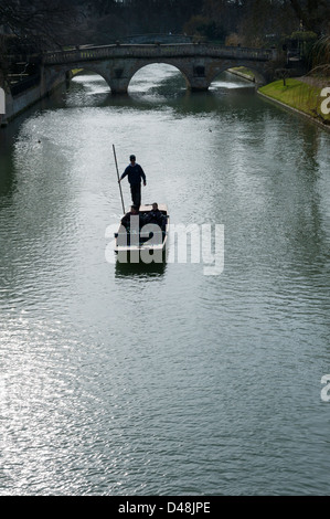 Punting in Cambridge on the River Cam. A punt chauffeur is silhouetted in spring sunshine with Clare Bridge in the background. Stock Photo