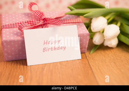 Pink wrapped present with bunch of white tulips and happy birthday card Stock Photo