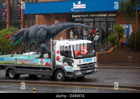 Bournemouth, UK. 8th March 2013. COMEDY Darren the dinosaur is released onto the streets of Bournemouth in aid of Comic Relief. Darren the dinosaur is three metres tall by eight metres long and was used in Walking with Dinosaurs, He was set free by celebrity Chris Jarvis from outside the BIC. The event was organised by Sainsbury's to encourage people to call into any store to get their red noses to protect themselves should they see the prehistoric creature while out and about. Credit:  Carolyn Jenkins / Alamy Live News Stock Photo