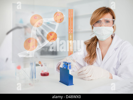 Chemist working in protective suit with futuristic interface showing DNA Stock Photo