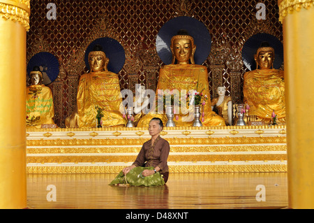 Meditating elderly Woman in front of Buddha Statues, Shwedagon Pagoda, Yangon, Myanmar Stock Photo