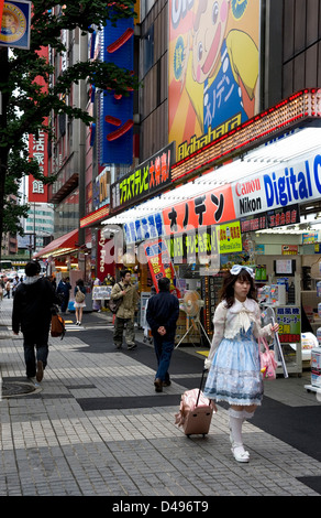 A girl wearing lolita style clothing walks down the sidewalk in the consumer electronics district of Akihabara, Tokyo. Stock Photo