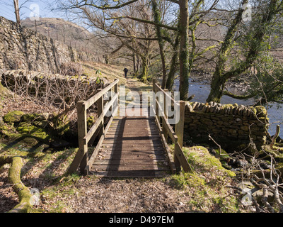 Riverside path and wooden footbridge along the Afon Glaslyn River in Nant Gwynant valley in Snowdonia National Park Stock Photo