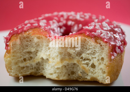 A horizontal image of a single doughnut, donut, with a bite out of it and with pink icing on a white plate Stock Photo