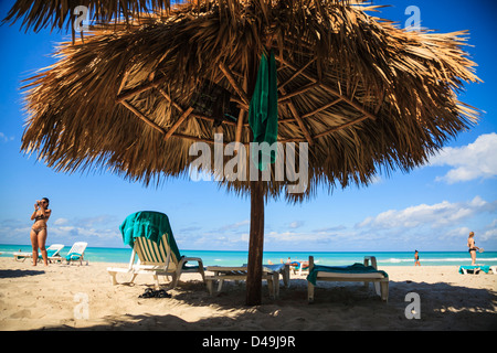 Varadero beach, Mantanzas, Cuba - woman in bikini taking pictures by a straw sun shelter and beach chairs Stock Photo