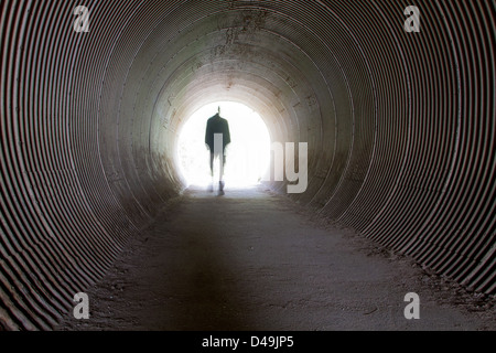 A single man walking through a tunnel into the light Stock Photo - Alamy