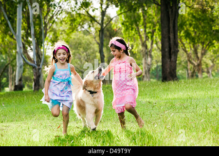 Two young girls running with golden retriever in park Stock Photo