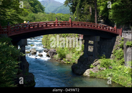 Visitors crossing the Futarasan Shrine Shinkyo sacred bridge over a clear water stream in Nikko, Tochigi, Japan.