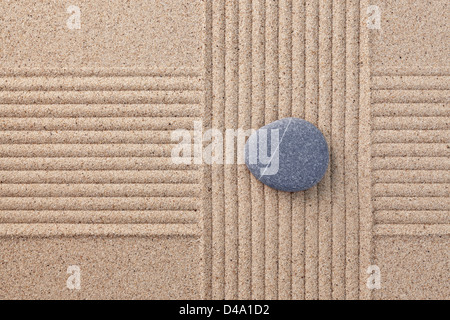 A single grey pebble on a raked sand zen garden with criss crossed sections Stock Photo