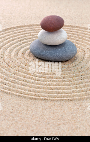 Three pebbles stacked on a circular raked zen garden Stock Photo