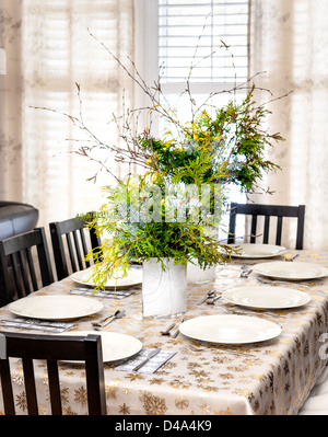 Dining table decorated for Christmas with eight place settings and evergreen centerpiece Stock Photo