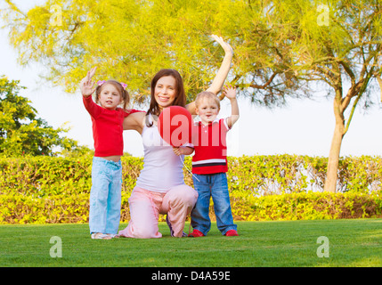 Photo of pretty mother with two cute kids raised hands up and enjoying sunny day, happy young family waving hand in spring park, Stock Photo