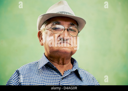 people and emotions, portrait of serious senior hispanic man with glasses and hat looking at camera against green background Stock Photo