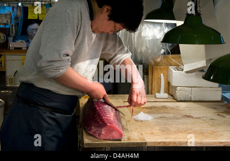 Fishmonger cuts and trims fresh raw tuna with sharp knife at Tsukiji Wholesale Fish Market, world's largest fish market in Tokyo Stock Photo