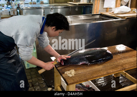 Fishmonger cuts fresh raw tuna with large sharp knife at Tsukiji Wholesale Fish Market, world's largest fish market in Tokyo Stock Photo