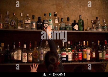 Waitress in front of shelves full of different alcoholic beverages bottles in the Minibar in Stuttgart, Germany at night Stock Photo