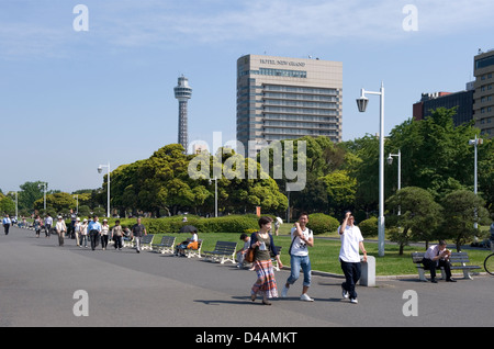 People enjoying a sunny day in Yamashita Koen Park along Yokohama City waterfront with Marine Tower dominating the skyline. Stock Photo