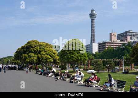 People enjoying a sunny day in Yamashita Koen Park along Yokohama City waterfront with Marine Tower dominating the skyline. Stock Photo