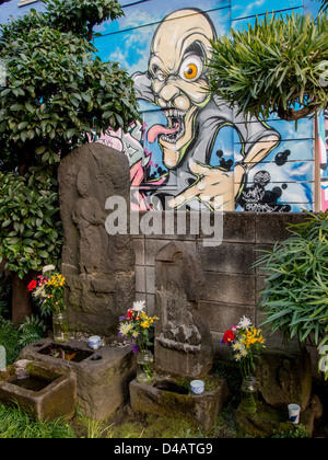 A graffiti monster looking down on buddhist statues in a small temple in Shibuya, Tokyo, Japan. Stock Photo