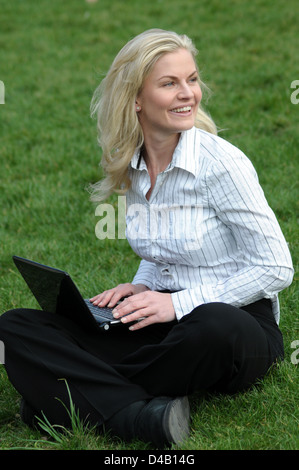 Woman sitting on the grass typing on her computer Stock Photo