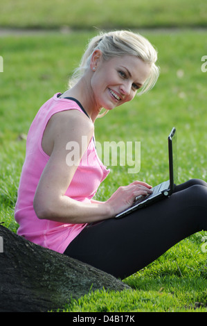 Woman sitting by a tree using her laptop computer in the park Stock Photo
