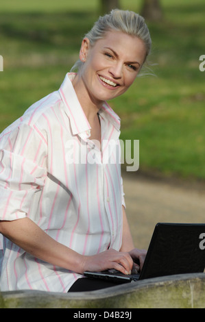 Woman sitting in a park working on a computer Stock Photo