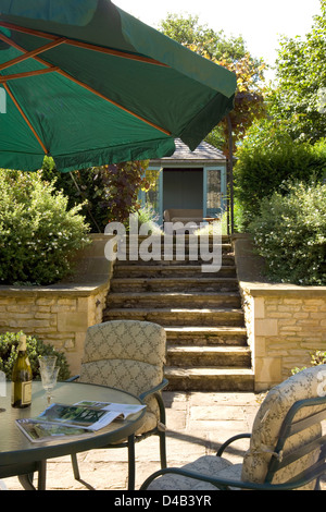UK gardens. Garden patio table and chairs with stone steps leading to a summer house.