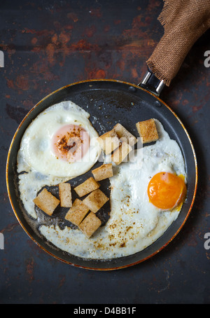 Frying pan full of scramble eggs from two eggs with a small pieces of toasted bread. Stands on grunge metal background. Stock Photo