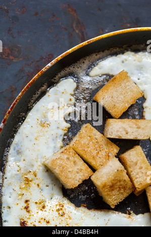 Frying pan full of scramble eggs from two eggs with a small pieces of toasted bread. Stands on grunge metal background. Stock Photo
