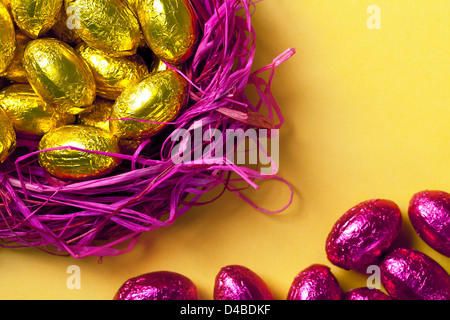 Chocolate easter eggs in pink nest. Holiday background. Selective focus on gold eggs. Top view Stock Photo
