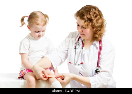 Girl with scratched knee. Doctor curing kid isolated on white. Stock Photo