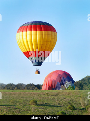Hot air balloons landing in green hills with trees Stock Photo