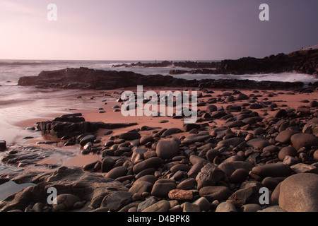 A scenic view of Ballito beach, Kwazulu Natal, warm colors of sunrise, boulders and sea sand in the foreground. Stock Photo