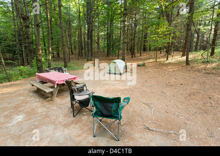 Campsite deep in the woods with a small size tent, picnic table, chairs, fire pit Stock Photo