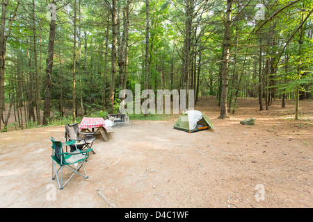 Campsite deep in the woods with a small size tent, picnic table, chairs, fire pit Stock Photo